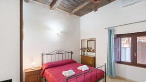 Un dormitorio con estructura metálica para la cama, una mesita de noche de madera con una lámpara, un aparador y una ventana con cortinas.