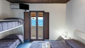 Una habitación con una cama litera, un escritorio con lámpara y vistas al mar a través de una puerta.