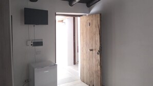 Une pièce avec une porte en bois, un appareil électroménager blanc et un téléviseur fixé au mur.