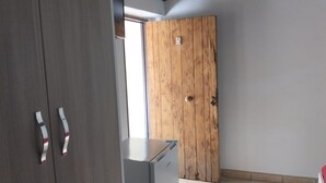 Une chambre avec une porte en bois, un petit réfrigérateur et une armoire dont les poignées sont rayées.