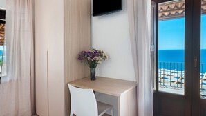 Ein Zimmer mit Schreibtisch, Stuhl, Wandfernseher und Meerblick durch eine Tür.
