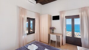 Ein Schlafzimmer mit Bett, Schreibtisch, Fernseher und einem Balkon mit Meerblick.
