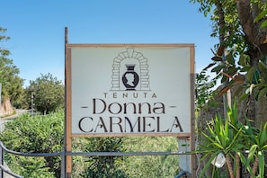 Opastekyltti, jossa lukee ”TENUTA Donna-CARMELA”, ja jossa on logo, jossa esiintyy maljakko ja sivukuva.
