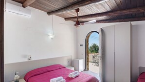 Una camera da letto con un letto, una ventola a soffitto, un condizionatore d'aria, un comodino, una lampada da notte, un armadio e vista attraverso un arco.
