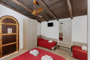 A room with two beds, a wooden door, a ceiling fan, a television, and a mirror. - Primula Room with Wi-Fi and Air Conditioning (Pisciotta)