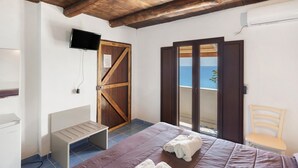 A bedroom with a bed, a TV, a wooden door, and a view of the sea. - Room 'Camera Palinuro Vista Mare' with Sea View, Wi-Fi and Air Conditioning (Pisciotta)