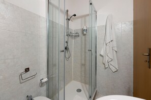 Cabina de bany amb envidriera, plat de dutxa amb aixeta manual, porta de vidre i tovallola penjada a la paret.