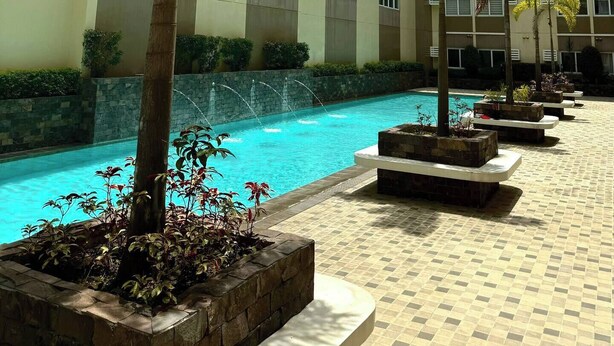 A modern building with a pool area, surrounded by palm trees and planters. - Calm and Clean Getaway + 400mbps+Netflix+Disney (Silang)