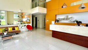 A modern reception area with a reception desk, a red chair, a sofa, and a large mirror. - Calm and Clean Getaway + 400mbps+Netflix+Disney (Silang)