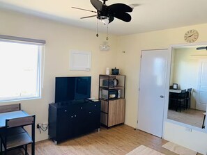 A compact living space with a ceiling fan, a flat-screen TV, a wooden cabinet, and a dining area with chairs. - Combined & Spacious Units+400mbps+Netflix+Disney (Silang)