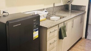 A compact kitchen with a black refrigerator, a granite countertop, and light wooden cabinets. - Z’s Cozy Place (Silang)