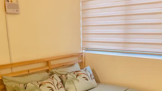 A single bed with a wooden frame, a light-colored mattress, and floral-patterned pillows. - Z’s Cozy Place (Silang)