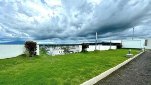 A rooftop terrace with a view of a cityscape, a white wall, and a paved walkway. - Z’s Cozy Place (Silang)