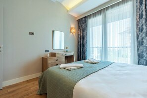 A hotel room with a bed, a nightstand, a mirror, a wall-mounted light, and a window with curtains.
