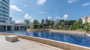A swimming pool with a curved design, surrounded by a landscaped area with palm trees and a gazebo. - Maxihomes Snitch (Antalya)