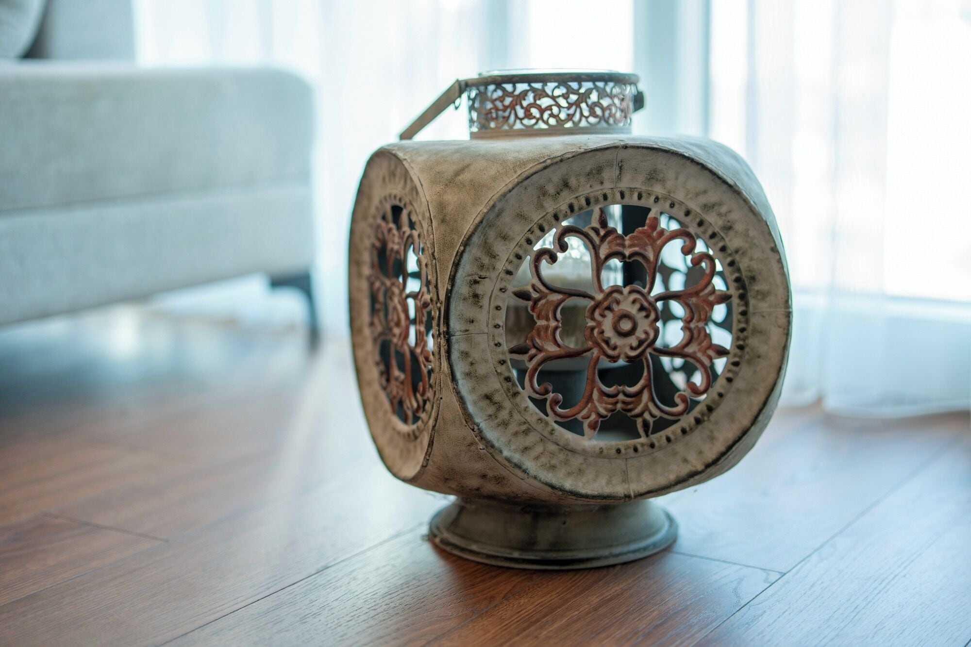 Un objeto metálico decorativo con diseños intrincados, posiblemente un farol, sobre un suelo de madera.