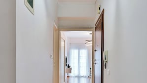 A hallway with a tiled floor, white walls, and a door at the end leading to a room with a window. - Porto Sea View Apartments - Ermou 61  (Thessaloniki)