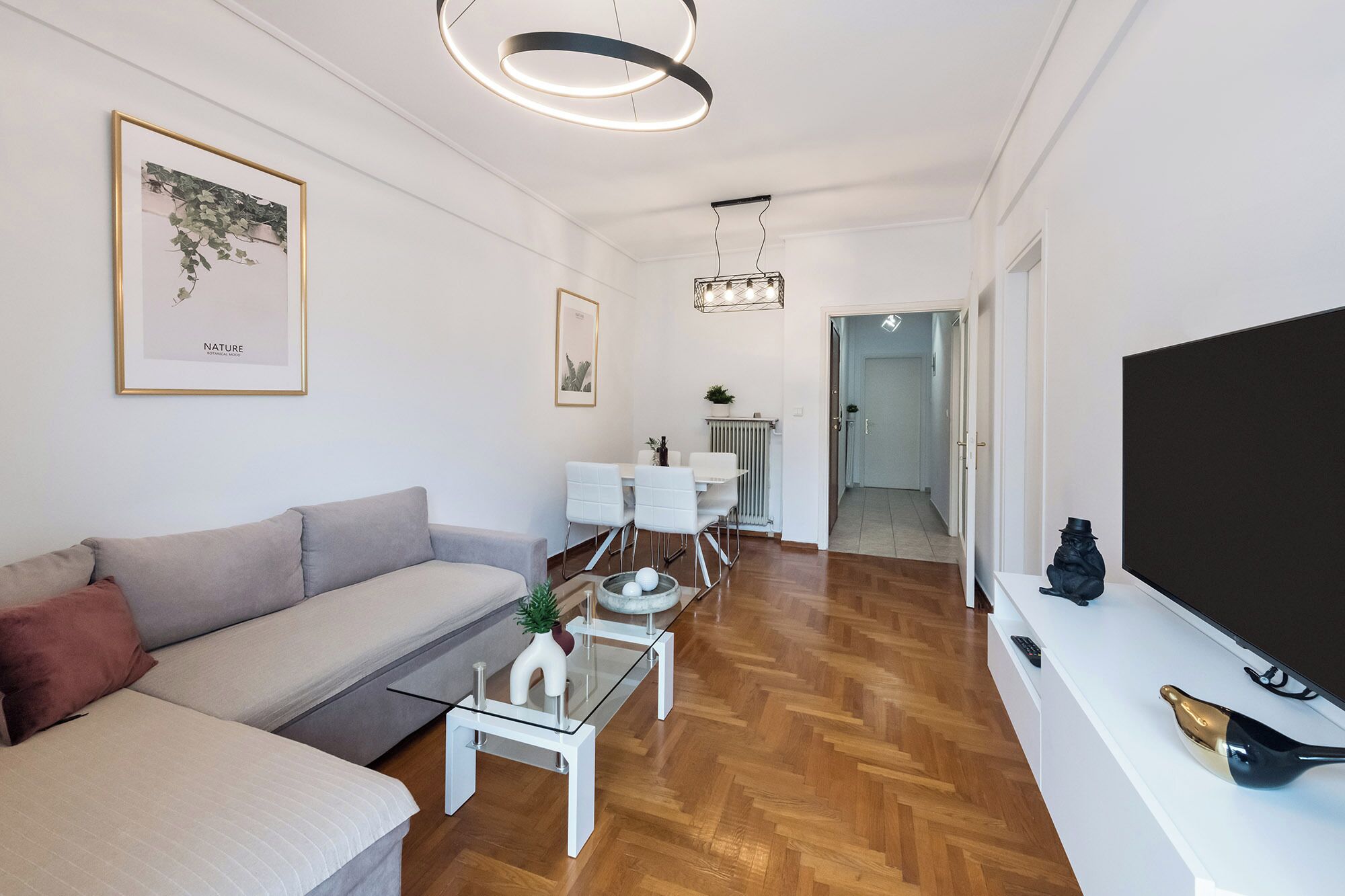 A modern living room with a sofa, a glass coffee table, a TV, and a dining area with a table and chairs.