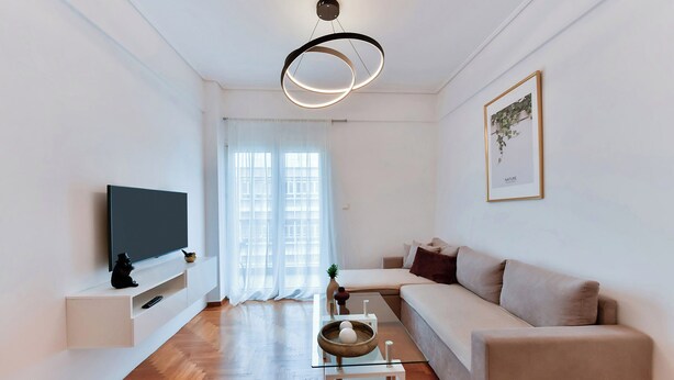 A modern living room with a flat-screen TV, a sofa, a coffee table, and a pendant light. - Porto Sea View Apartments - Ermou 61  (Thessaloniki)