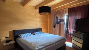 A bedroom with a wooden ceiling, a bed with white bedding, a nightstand, a dresser, and a television. - Apartment 'Ferienwohnung Sußebach mit 80 qm' (Vöhringen)