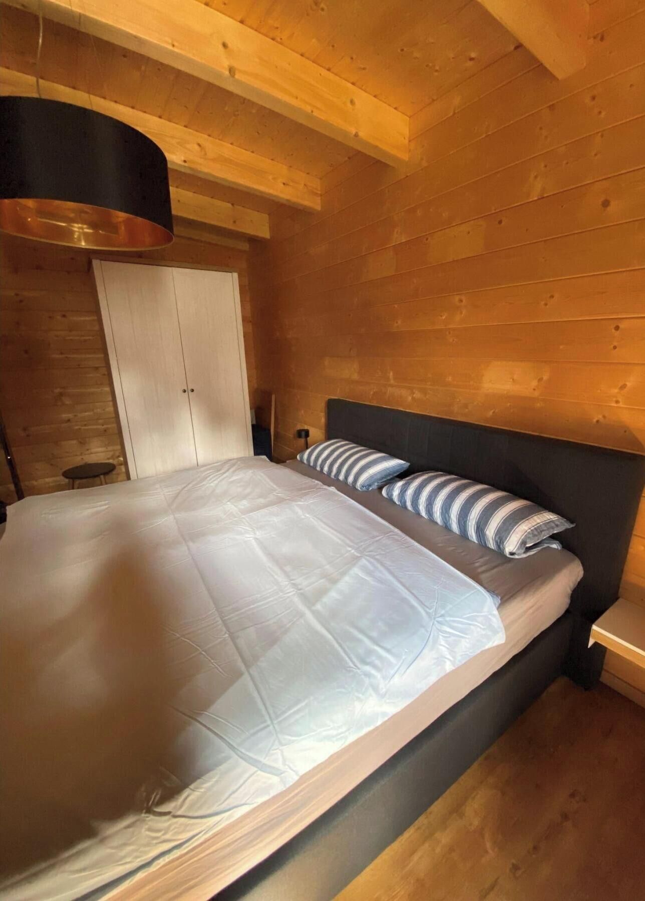 A bedroom with a bed, a nightstand, a lamp, and a wooden ceiling.