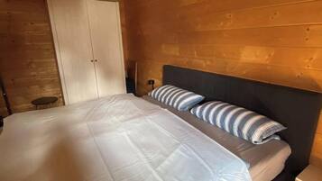 A bedroom with a bed, a nightstand, a lamp, and a wooden ceiling.
