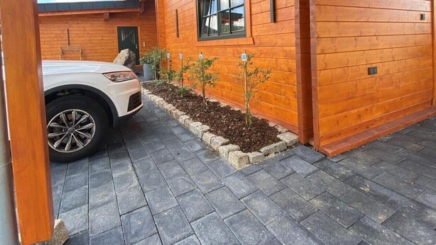 A wooden building with a covered driveway, a car parked in front, and a small garden area. - Apartment 'Ferienwohnung Sußebach mit 80 qm' (Vöhringen)