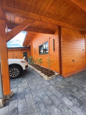 Un bâtiment en bois avec une allée couverte, une voiture garée devant et un petit jardin.