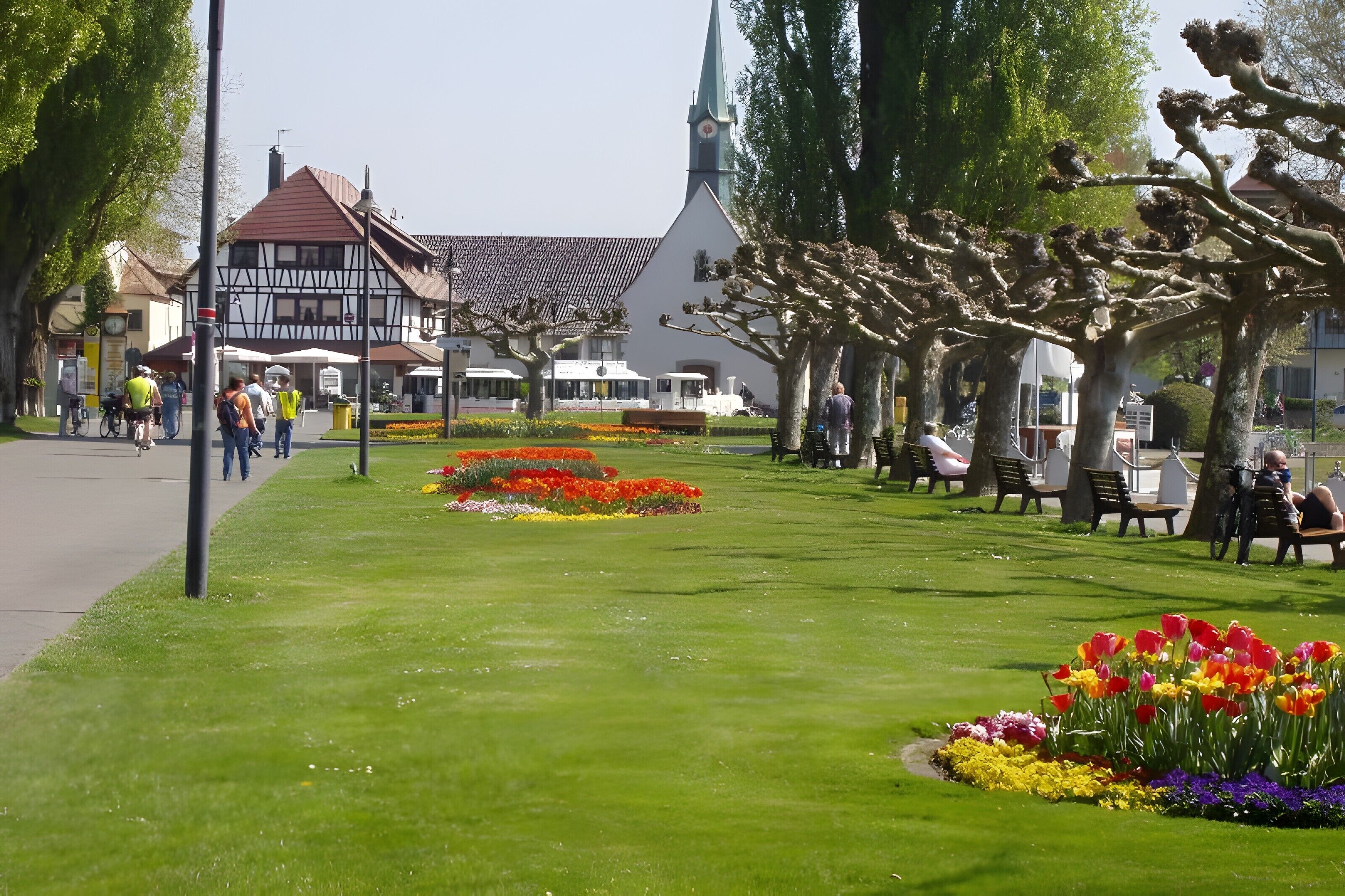 Ein Stadtplatz mit einer Kirche, Bänken und Blumenbeeten.