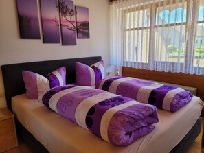 Una cama doble con ropa de cama púrpura y blanca, un cabecero oscuro y tres cuadros colgados en la pared.