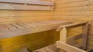 Un sauna avec des bancs en bois et un récipient en métal, probablement destiné à contenir de l’eau ou de la vapeur.
