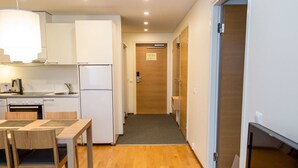 Une cuisine compacte dotée d’appareils électroménagers modernes, un coin repas avec une table et des chaises, et un couloir menant à une porte.