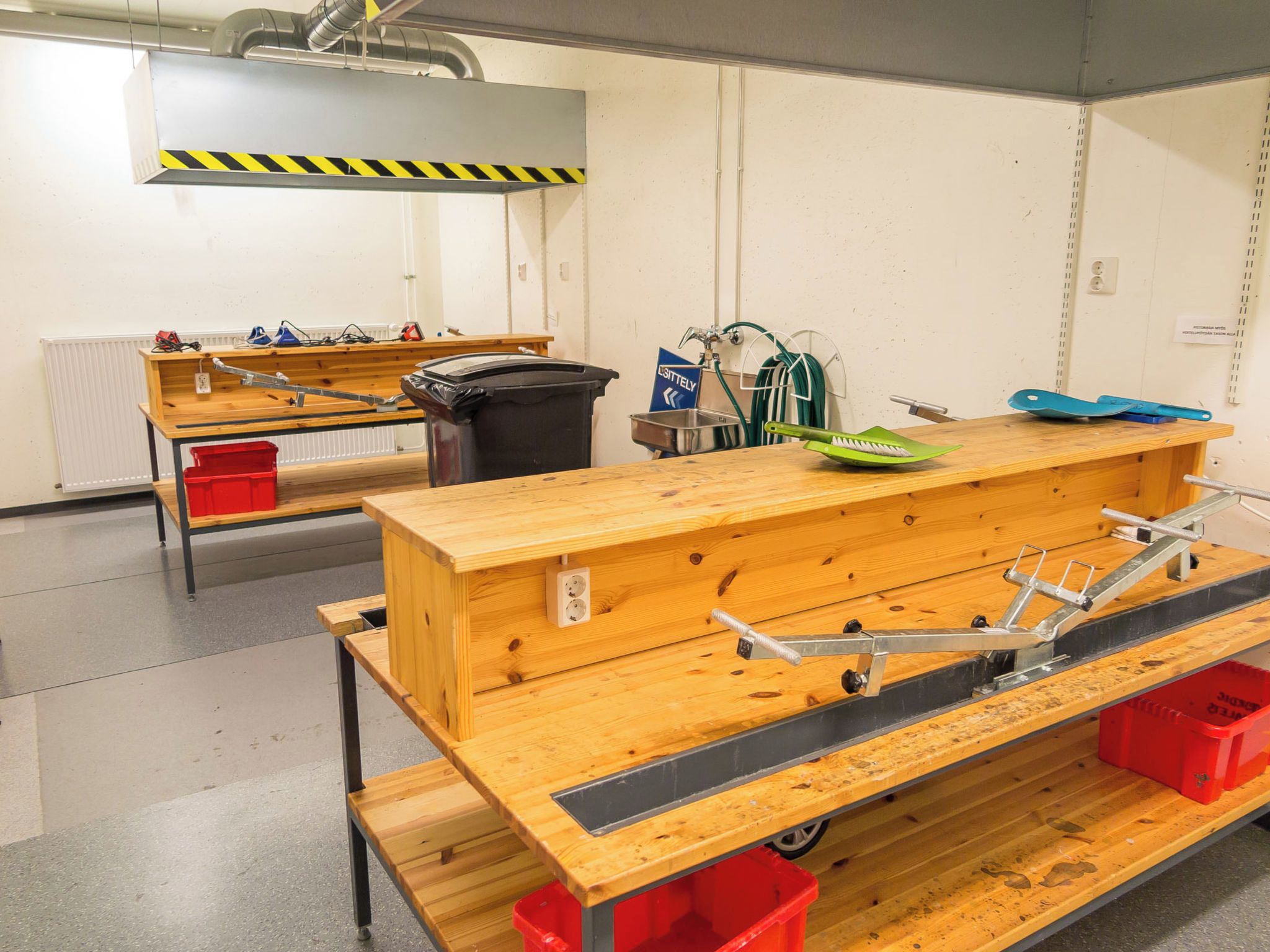 Een werkplaats met werkbanken, gereedschap en een afvalbak.