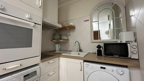 A compact kitchen with a microwave, oven, and washing machine. - Rooms Rey junto a Plaza España (Madrid)