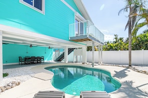 Uma casa turquesa com piscina, móveis de jardim e cerca branca.
