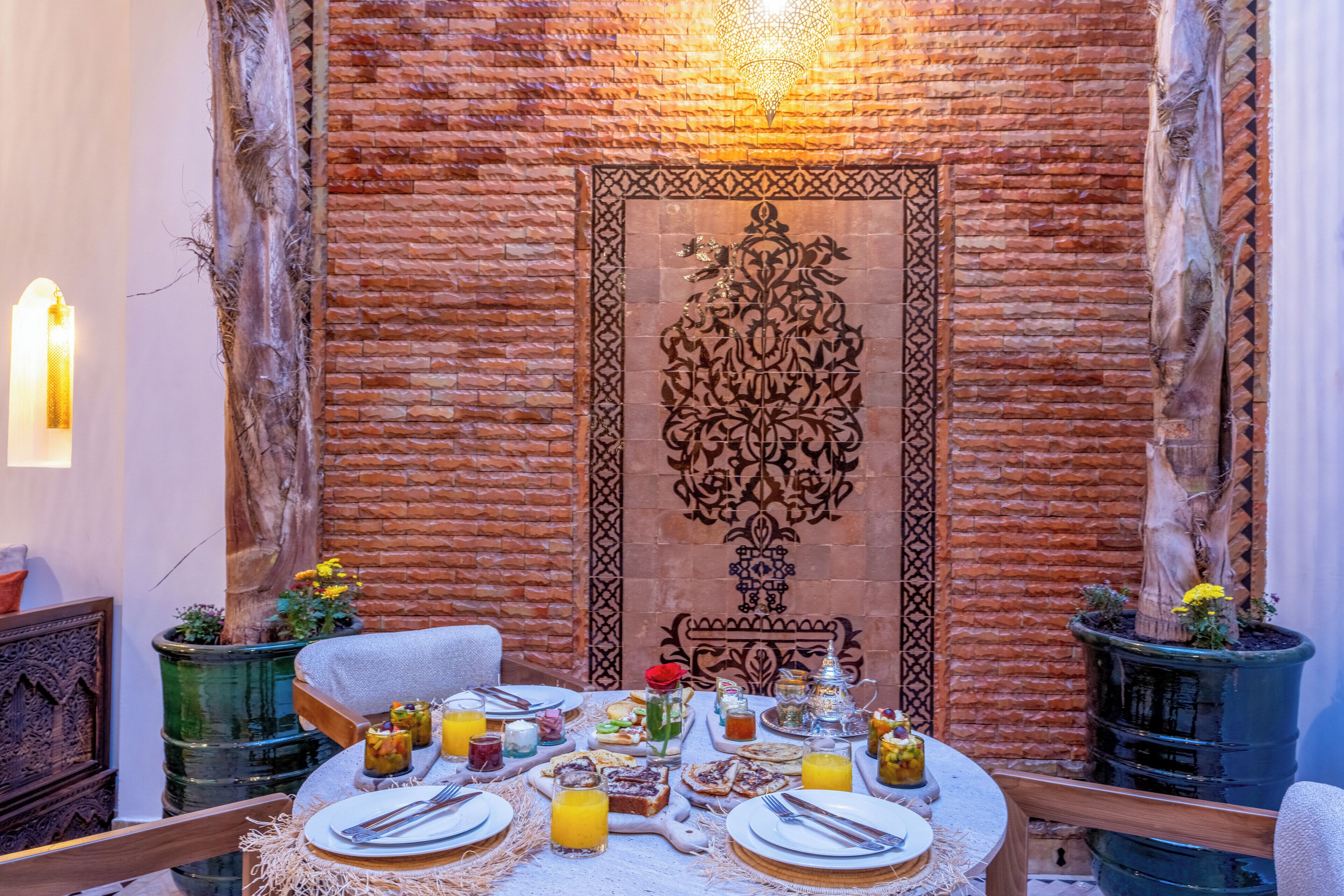 Una mesa de comedor dispuesta con platos, cubiertos y una variedad de comida y bebidas, rodeada de una pared de ladrillo y elementos decorativos.