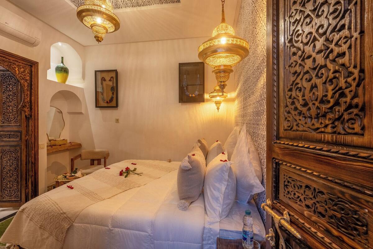 Una habitación tradicional marroquí con cama, puerta de madera ornamentada e iluminación decorativa.