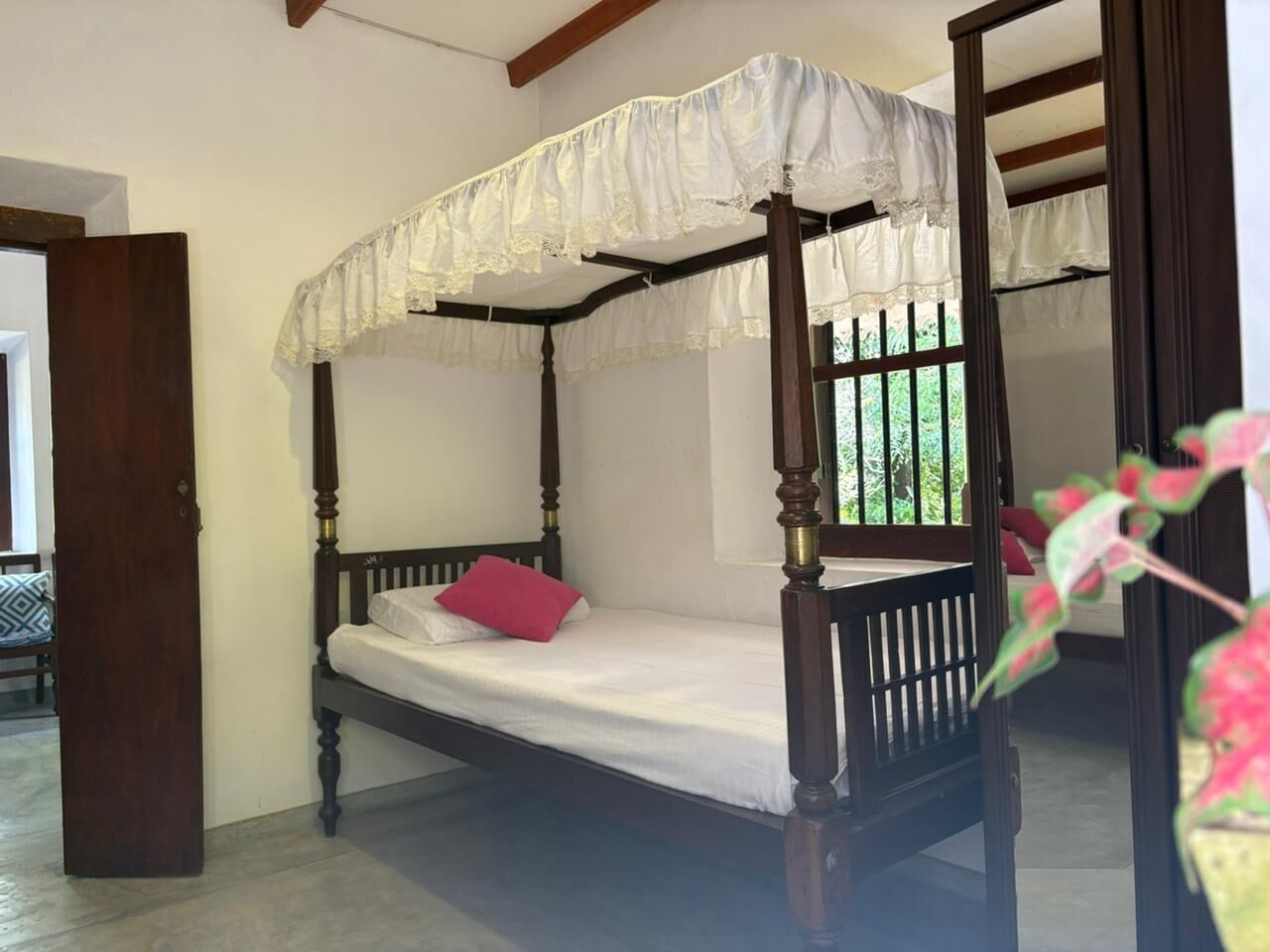 A four-poster bed with a white canopy and a single red pillow.