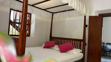 Un lit à baldaquin avec des draps blancs et des oreillers roses, une tête de lit en bois et un dais en dentelle.