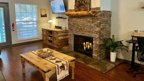 A living room with a stone fireplace, a television mounted above it, a wooden coffee table, and a potted plant. - Golf-Course View Retreat w/ Fireplace & Patio (Ruidoso)