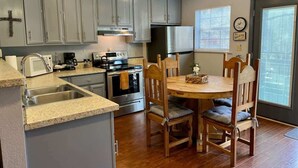 A kitchen with grey cabinets, a stainless steel refrigerator, a stove, and a dining table with wooden chairs. - Golf-Course View Retreat w/ Fireplace & Patio (Ruidoso)