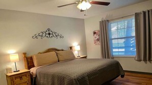 A bedroom with a bed, nightstands, a ceiling fan, a window with curtains, and a wall decoration. - Golf-Course View Retreat w/ Fireplace & Patio (Ruidoso)