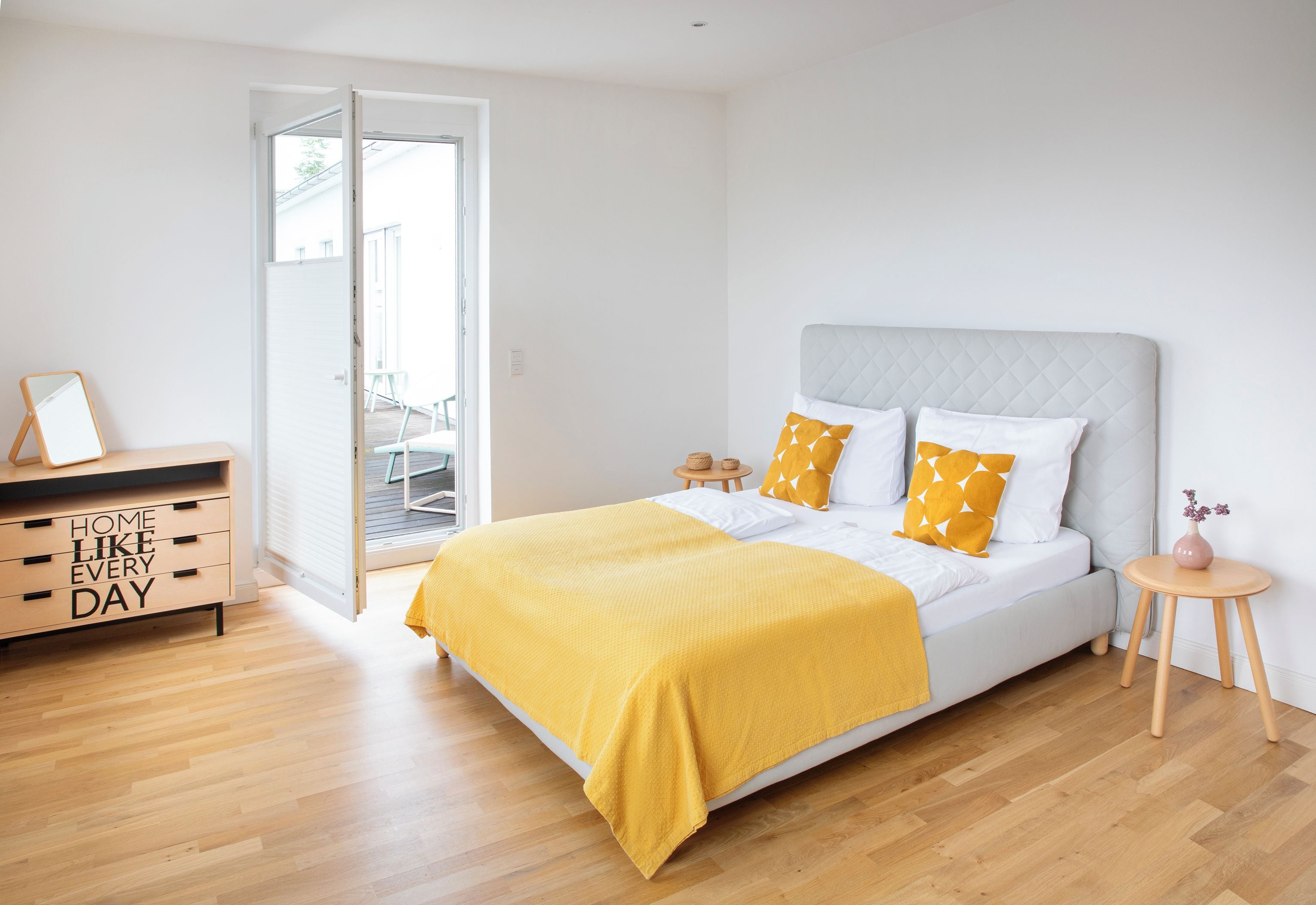 Ein Schlafzimmer mit einem Bett, einer Kommode, einem kleinen Tisch und einer Tür zu einem Außenbereich.