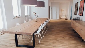 A modern dining area with a long wooden table, white chairs, and pendant lighting. - Louis & Louise Apartments & Penthouses  (Bremen)