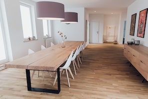 A modern dining area with a long wooden table, white chairs, and pendant lighting. - Louis & Louise Apartments & Penthouses  (Bremen)