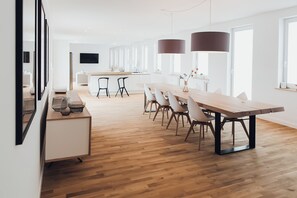 A modern kitchen with a wooden dining table, chairs, and pendant lights.