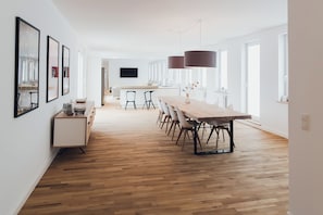 A spacious kitchen with a long wooden table, modern pendant lights, and a flat-screen TV mounted on the wall. - Louis & Louise Apartments & Penthouses  (Bremen)
