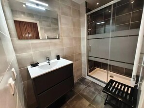 Ein modernes Badezimmer mit Waschtisch, Duschkabine aus Glas und einer kleinen Sitzbank.