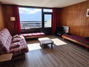 Ein Wohnzimmer mit einer Couch, einem kleinen Tisch, einem Fernseher und Meerblick durch große Fenster.