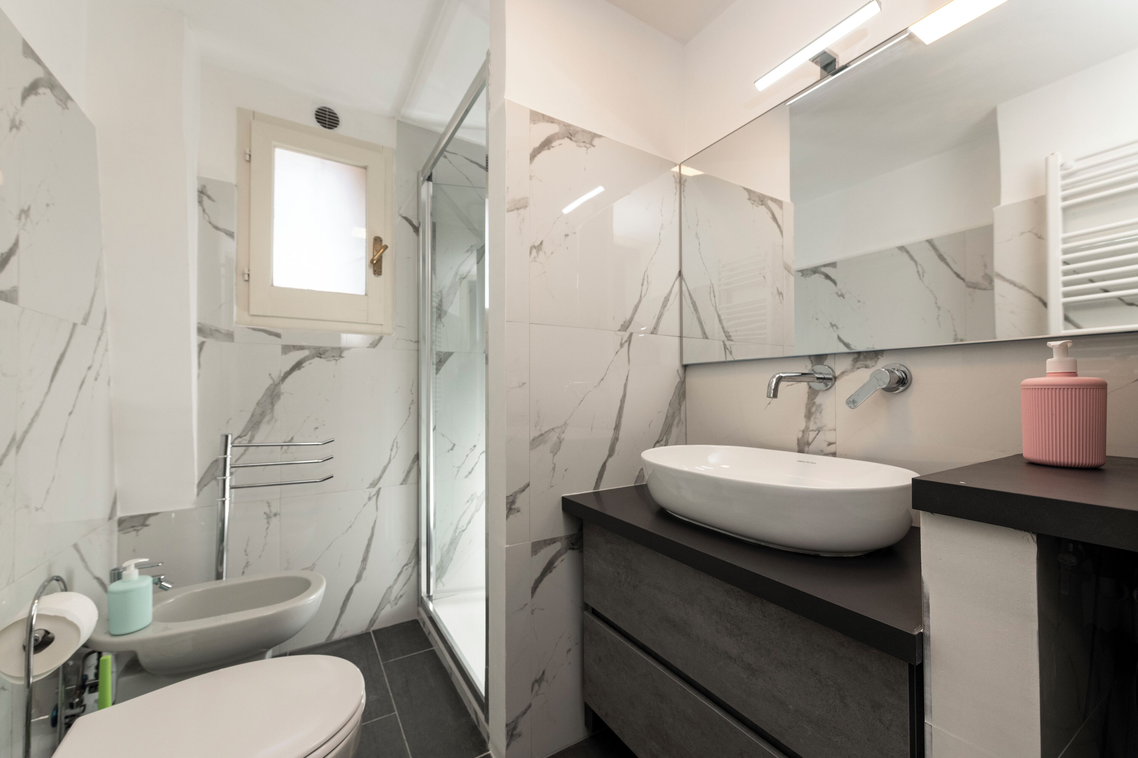 A modern bathroom with a glass shower enclosure, a white sink, and a black vanity.